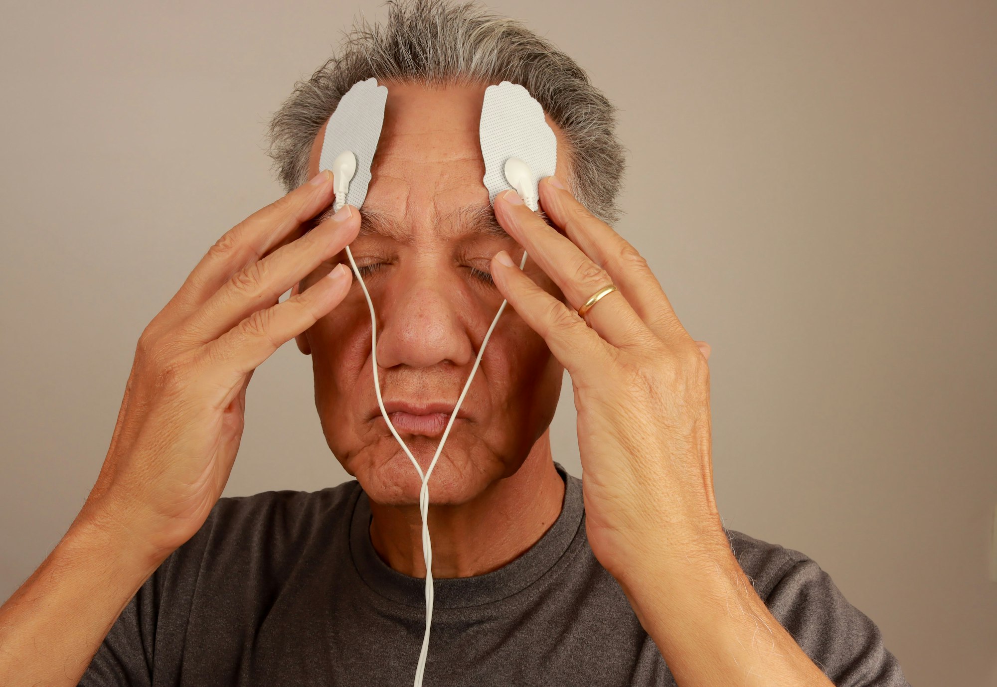 Senior man using electrical stimulation pads on forehead f