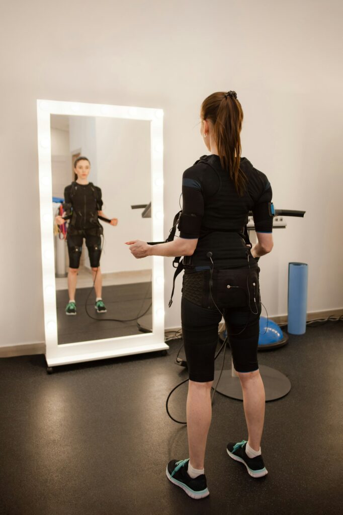 Sporty woman in electrical muscular stimulation suit doing exercise in gym