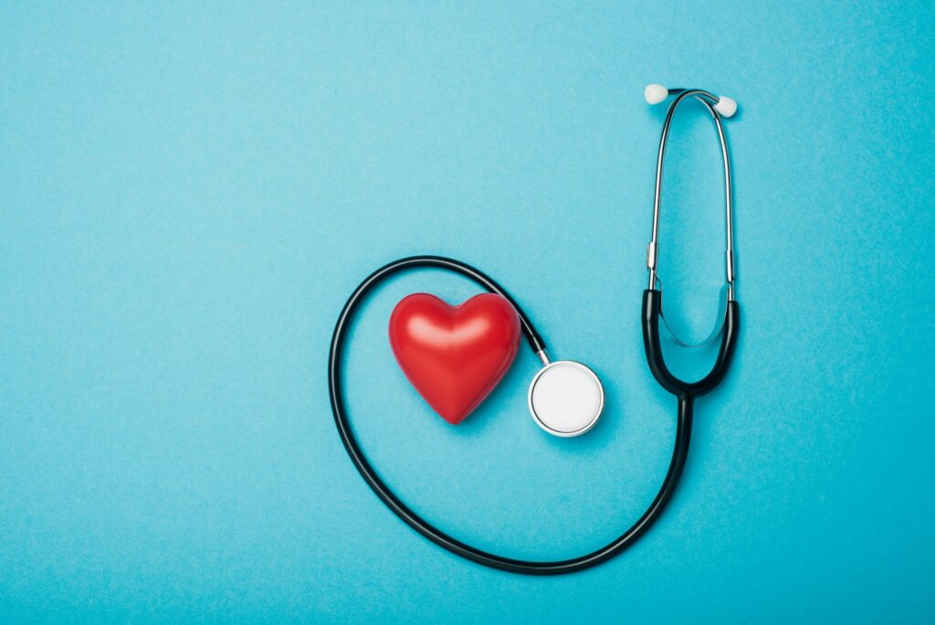 Top view of decorative heart and stethoscope on blue background, world health day concept